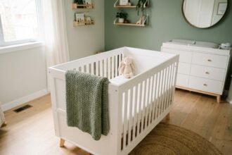 Chambre bébé design moderne avec lit à barreaux blanc en bois scandinave, tapis jute et mur vert sauge
