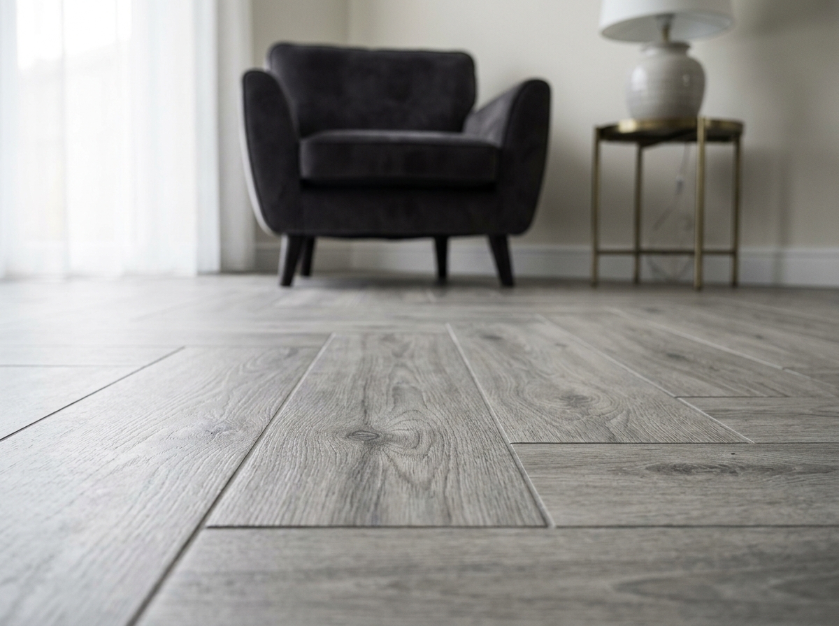 Détail d'un sol effet bois gris en chevrons dans un salon contemporain avec fauteuil velours anthracite