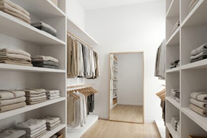 Dressing blanc moderne avec étagères ouvertes, vêtements rangés par couleur et paniers en osier pour une chambre organisée et fonctionnelle