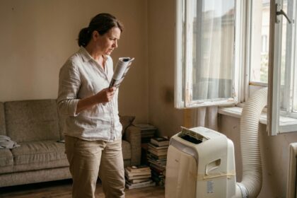 Femme d'âge mûr regardant une vieille climatisation portable dans un appartement, illustrant les limites des clims portables