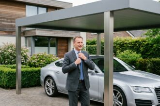 Homme d'affaires ajustant sa cravate près d'une voiture sous un carport moderne