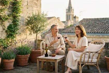 Couple bordelais se relaxant sur une terrasse en bois avec mobilier en rotin et plantes méditerranéennes