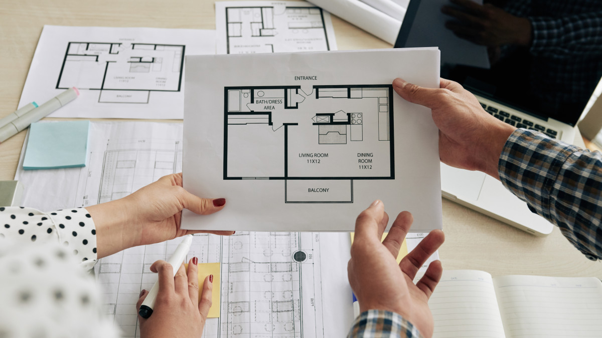 un plan de maison tenu entre les mains de professionnels de la construction